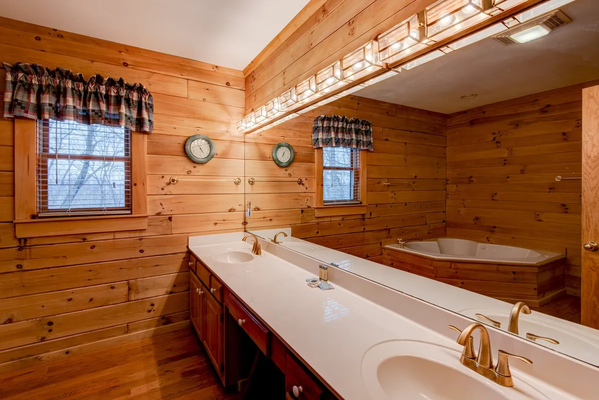 A spacious bathroom features a double vanity with sinks, a luxurious bathtub, and wood-paneled walls. Natural light streams in through windows, creating a spa-like ambiance ideal for relaxation and rejuvenation.