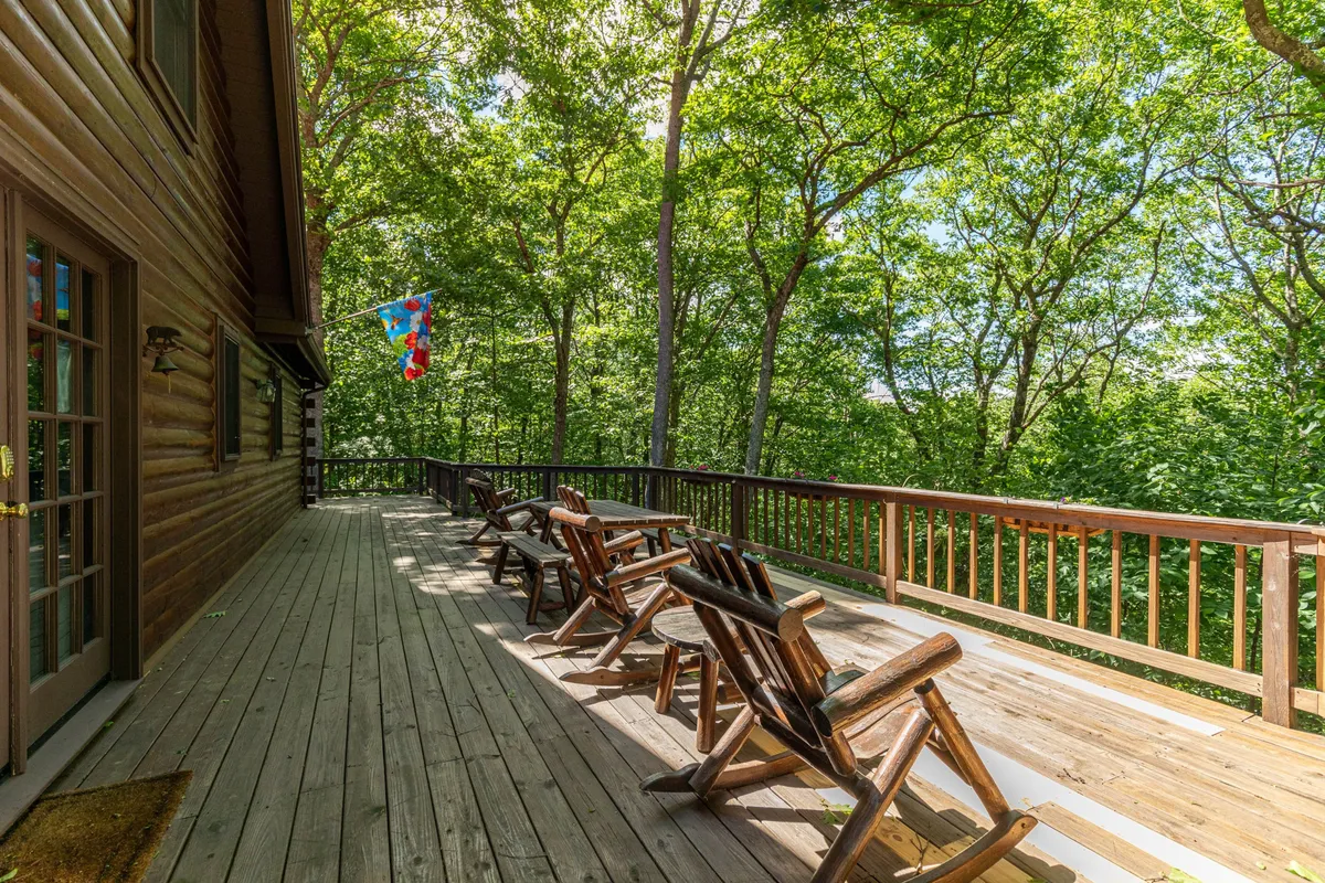 A peaceful wooden deck surrounded by lush trees, displaying a colorful flag and a picnic table. The setting invites guests to enjoy meals outdoors, soak in the mountain air, and relax in a natural sanctuary. The image captures the essence of year-round mountain living in a pet-friendly environment.