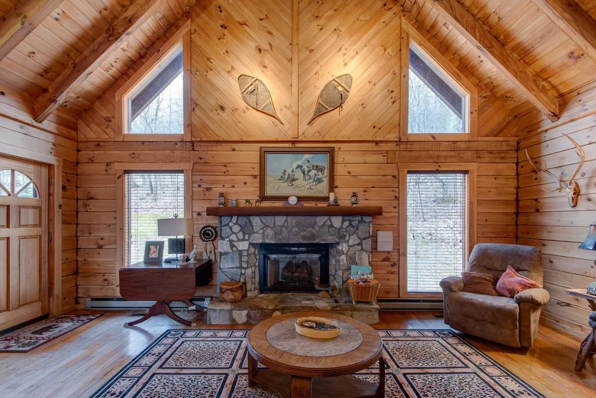 A cozy, inviting living room with a striking stone fireplace, rustic wooden walls, large windows letting in natural light, and a comfortable seating area. The ambiance is warm and intimate, ideal for quiet evenings spent together by the fire after exploring downtown or enjoying outdoor adventures.