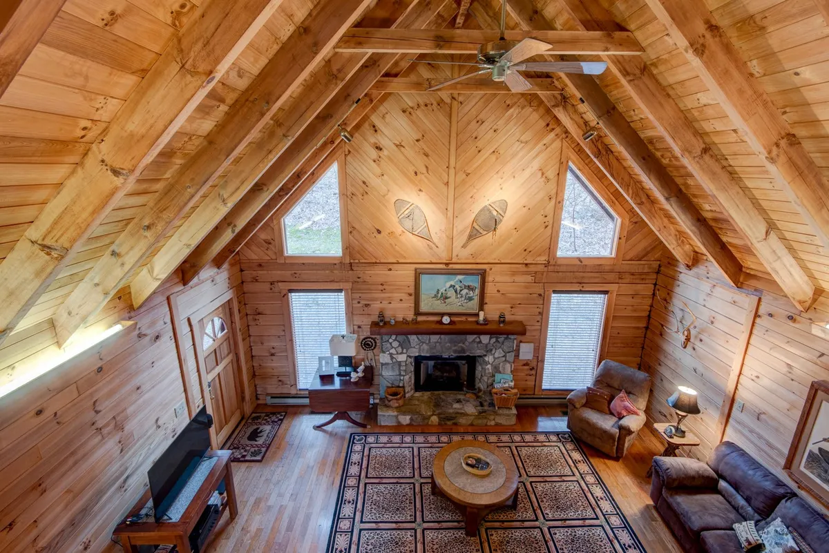 A spacious living area with wooden ceiling beams, a grand stone fireplace, a central coffee table, and expansive windows showcasing outdoor scenery. The interior’s layout encourages gathering while maintaining a strong connection to the exterior environment, reinforcing the sense of escape and adventure.