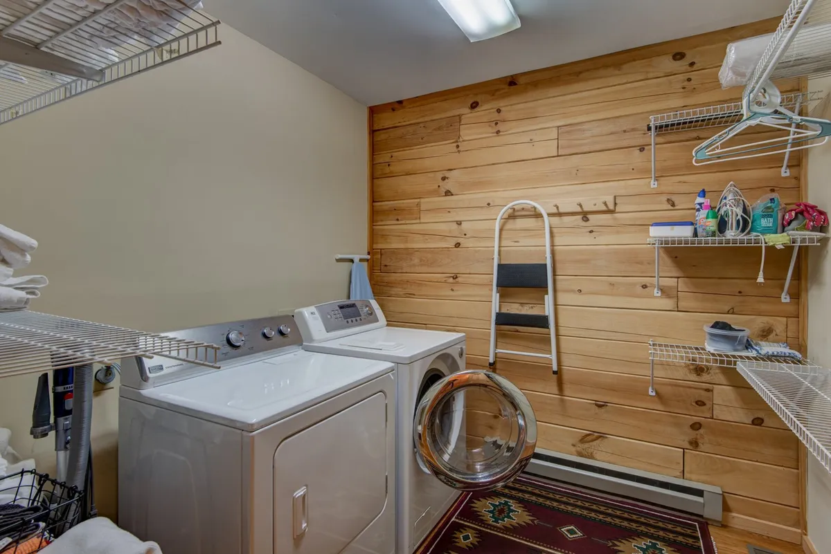 A practical laundry room with a washing machine, drying rack, and wood-paneled walls. The space is tidy and functional, conveniently located for guest use.