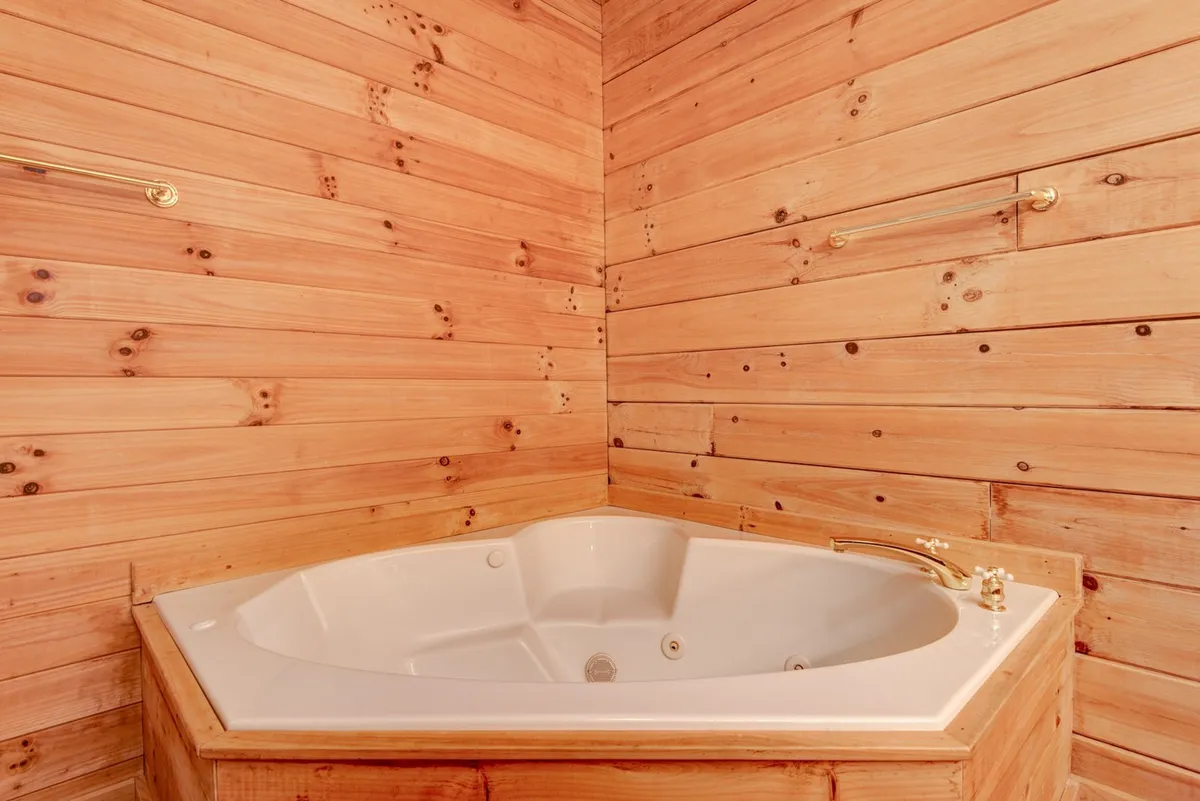 A tranquil bathroom space featuring a luxurious Jacuzzi tub set against rich wooden walls, with elegant gold fixtures. The intimate, spa-like atmosphere is ideal for couples seeking relaxation and special moments together after a day of mountain exploration.