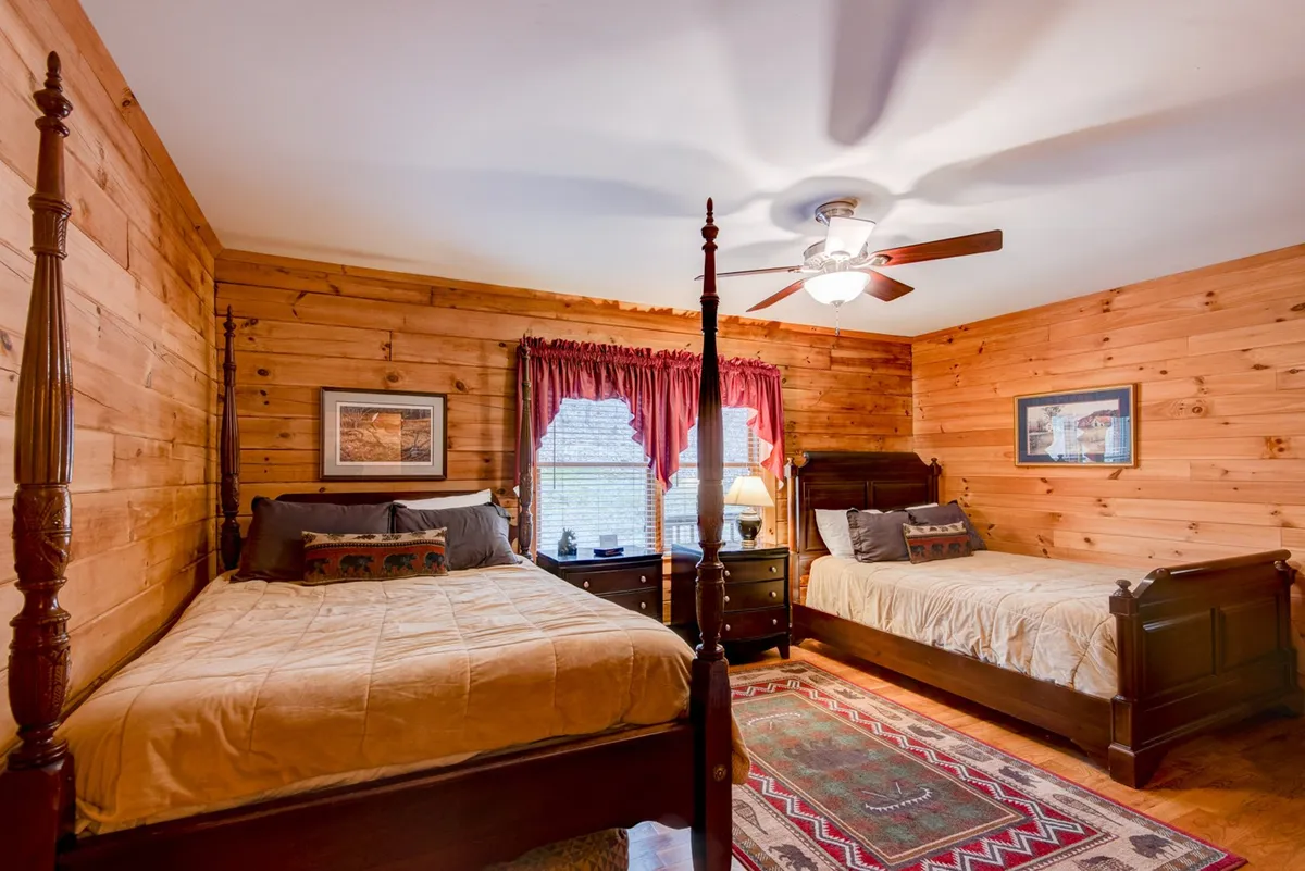 A cozy guest bedroom with two wooden beds, a decorative rug, and a nightstand with a lamp. The warmth of wood paneling and soft lighting creates a welcoming environment perfect for families or friends.